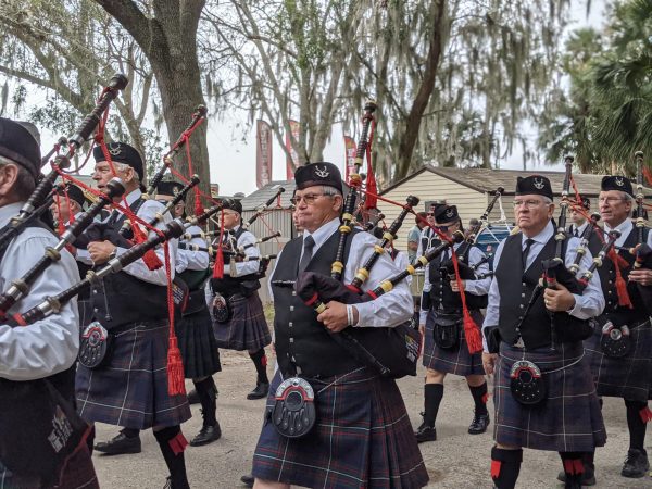 The parade of pipers march through the forest road in front of the tents and booths.