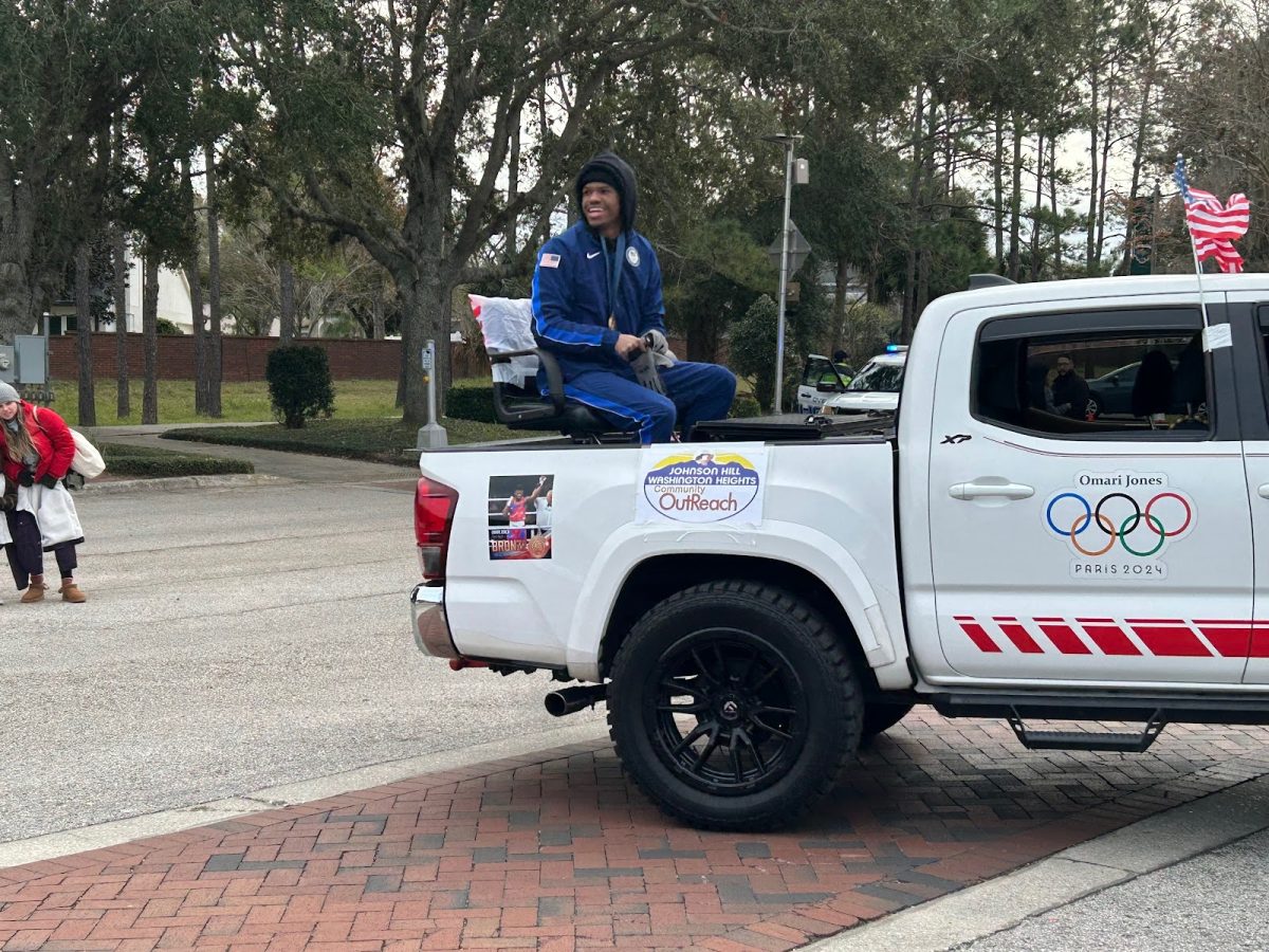 Omari Jones sits on the back of the Johnson Hill Washington Heights Community Outreach truck. The Olympian wears the classic blue tracksuit and his bronze medal around his neck.