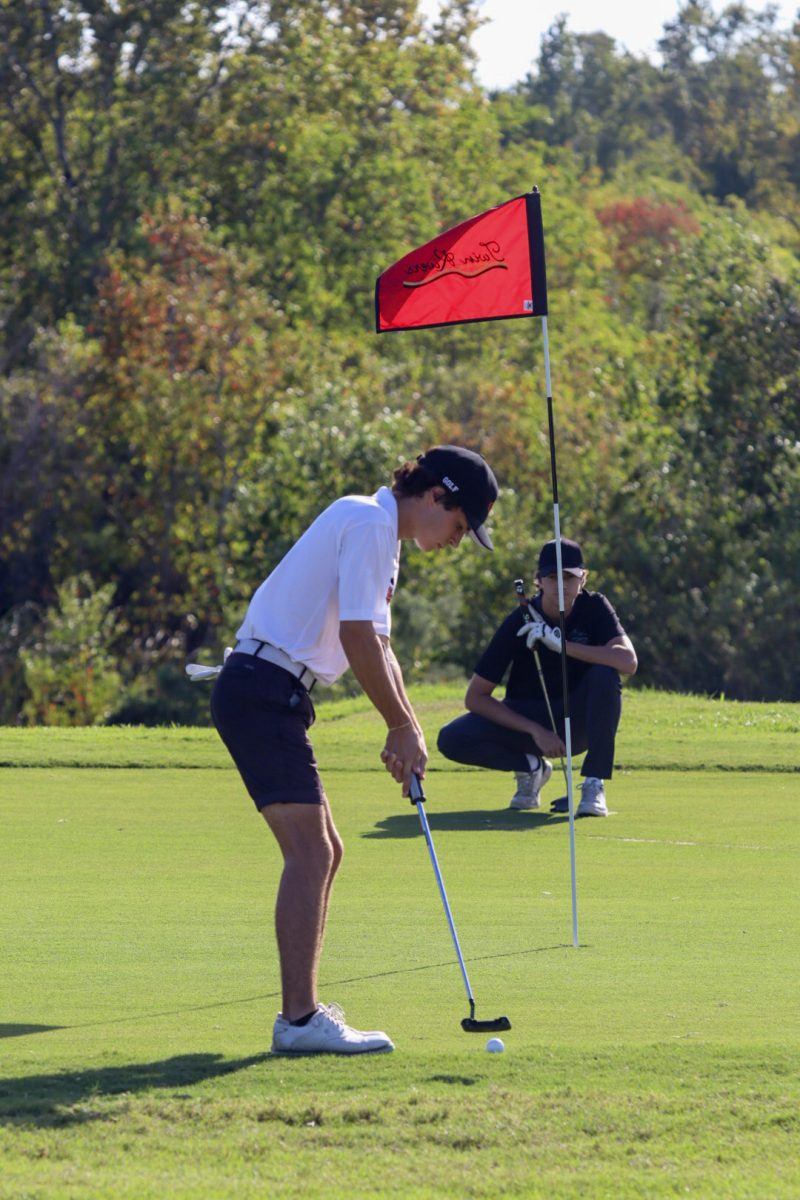 Tre Dahm, senior, crouches slightly, facing his club and golf ball near the hole.