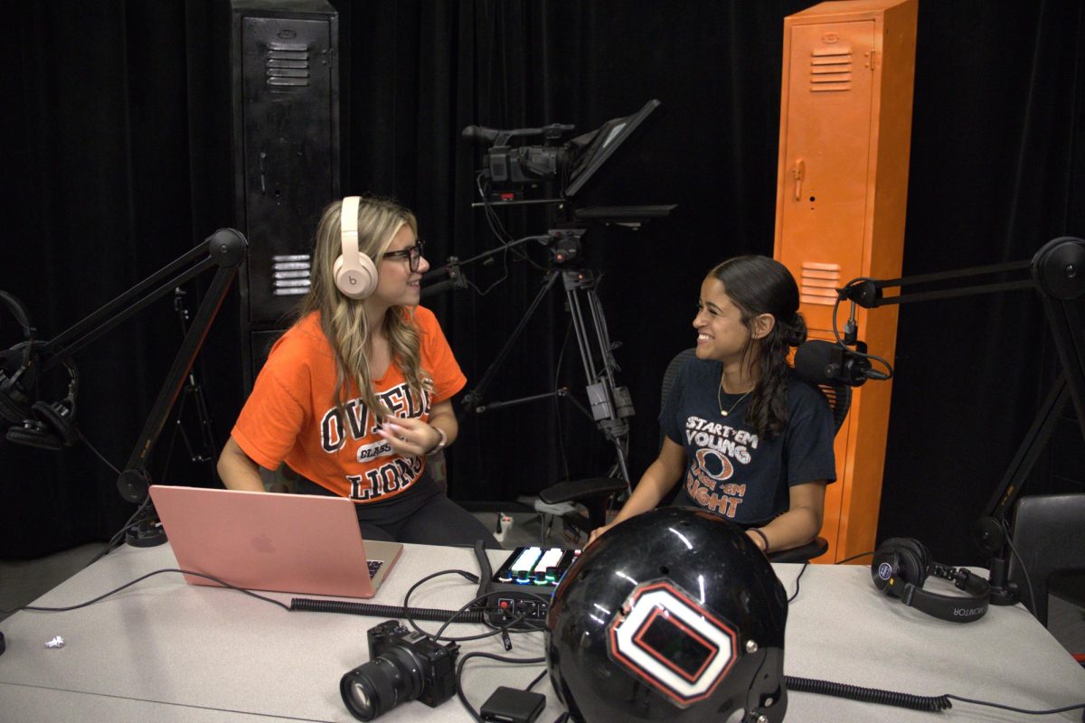 Smiling and sitting across from each other, Gabriella Decesare and Samantha Lebron sit with their audio setup for recording. 