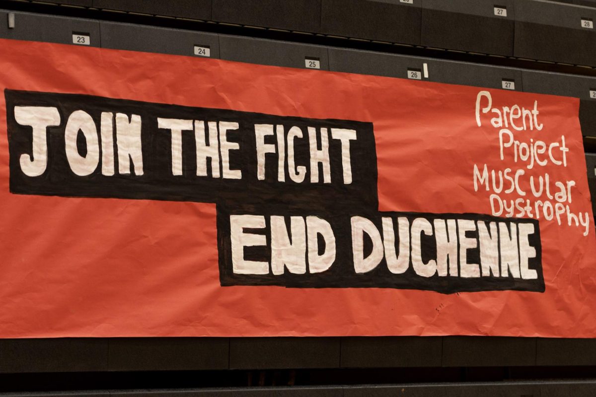 An orange hand-painted poster hangs from the pews of bleachers in the gym describing what the fundraiser is fighting for.
