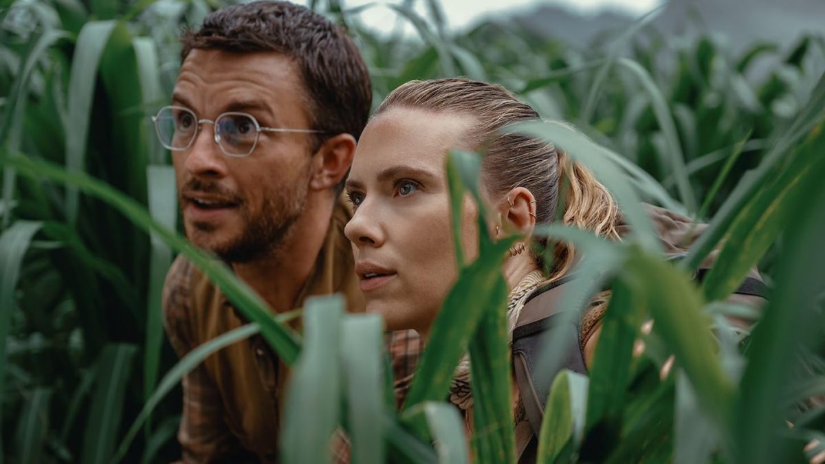 Dr. Henry Loomis (Jonathan Bailey) and Zora Bennett (Scarlett Johansson) hide in the grass to observe a dinosaur in "Jurassic World Rebirth." Image courtesy of Universal Pictures.
