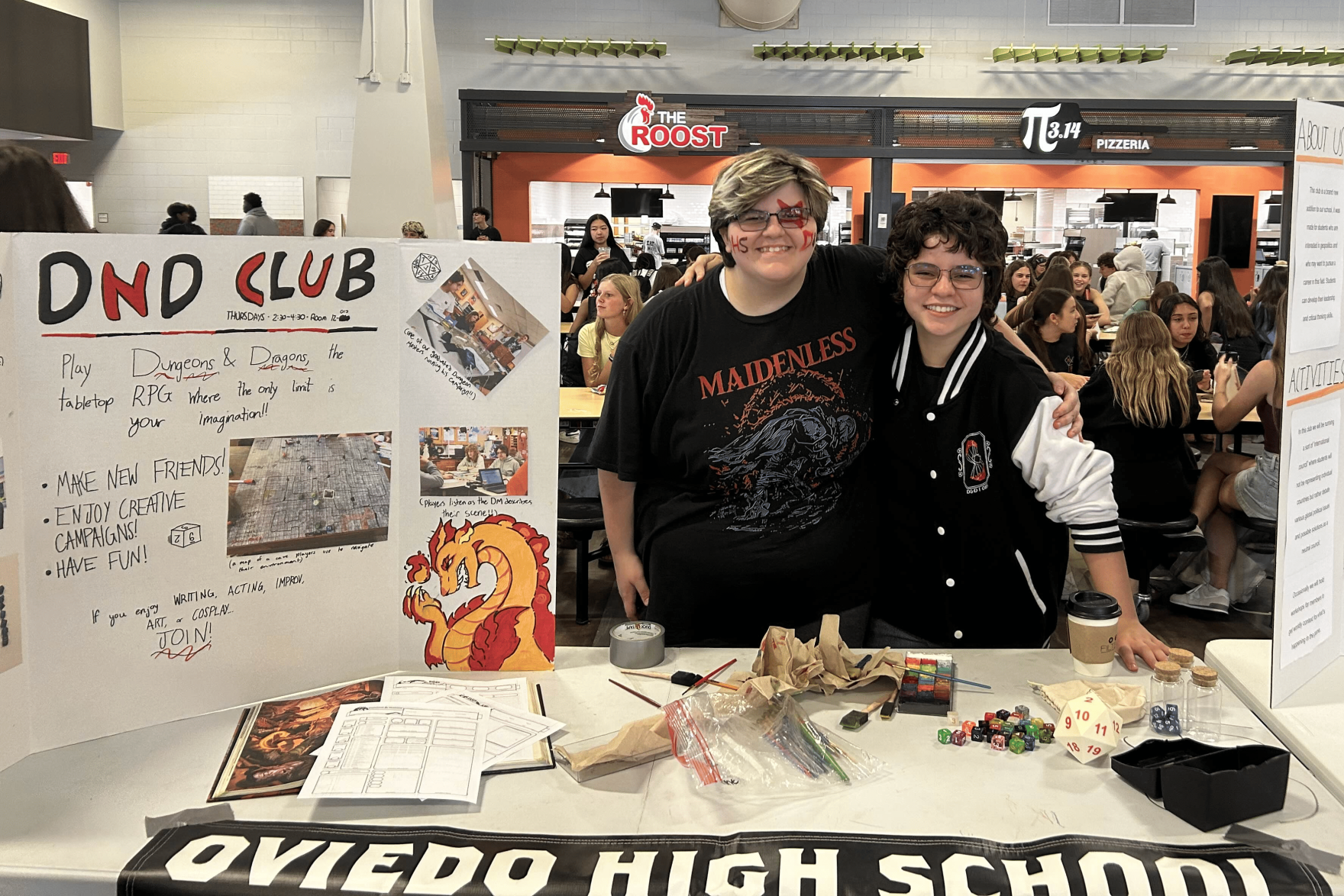 At Club Crawl on Wednesday, Sept. 3, club president Em Martinez (11) and vice president Cal Culhane (11) smile for a photo, arm in arm, next to a tri-fold board promoting the club. Martinez and Culhane took over the club after its previous president graduated. Image courtesy of Noah Hedlund.
