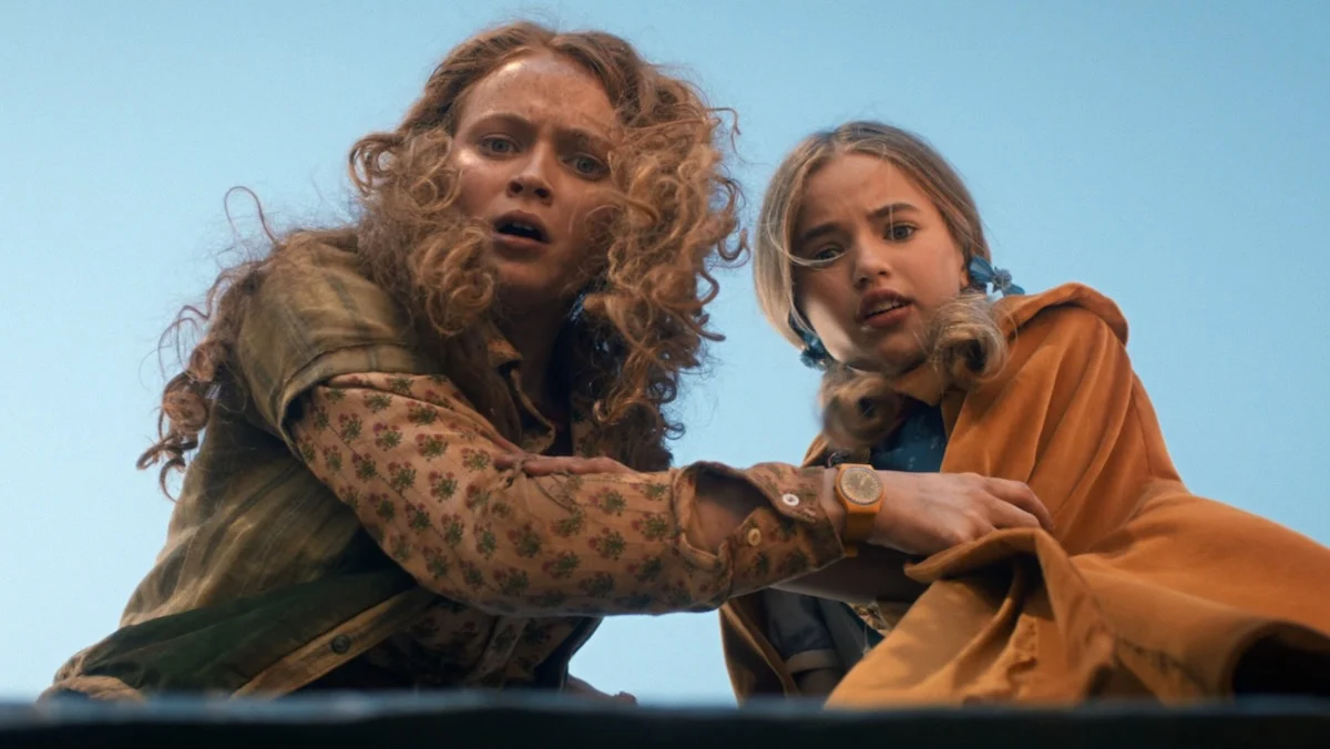 During their daring escape from "Camazotz," Vecna's (Jamie Campbell Bower) mind, Holly Wheeler (Nell Fisher) and Max Mayfield (Sadie Sink) stare in shock at a hidden trapdoor. Image courtesy of Netflix.