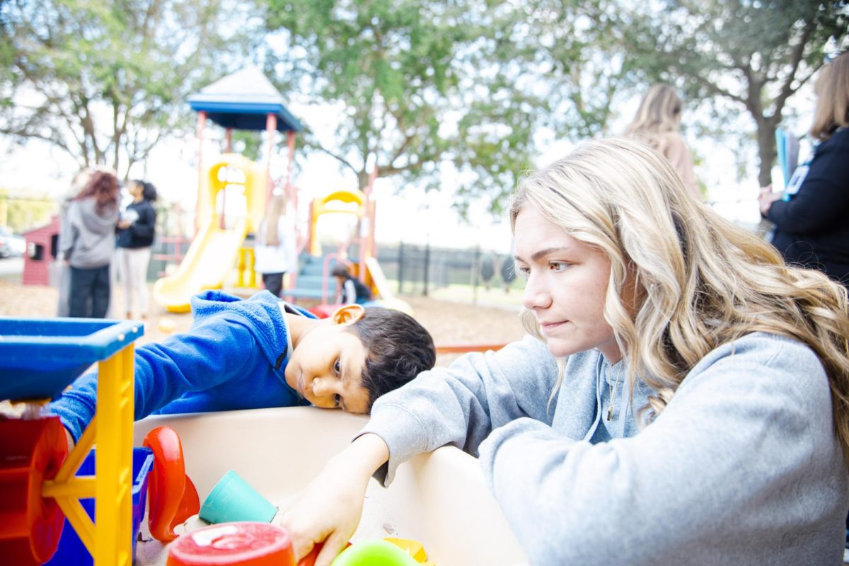 ** joins one of the kids reaching inside a sand and water play table.