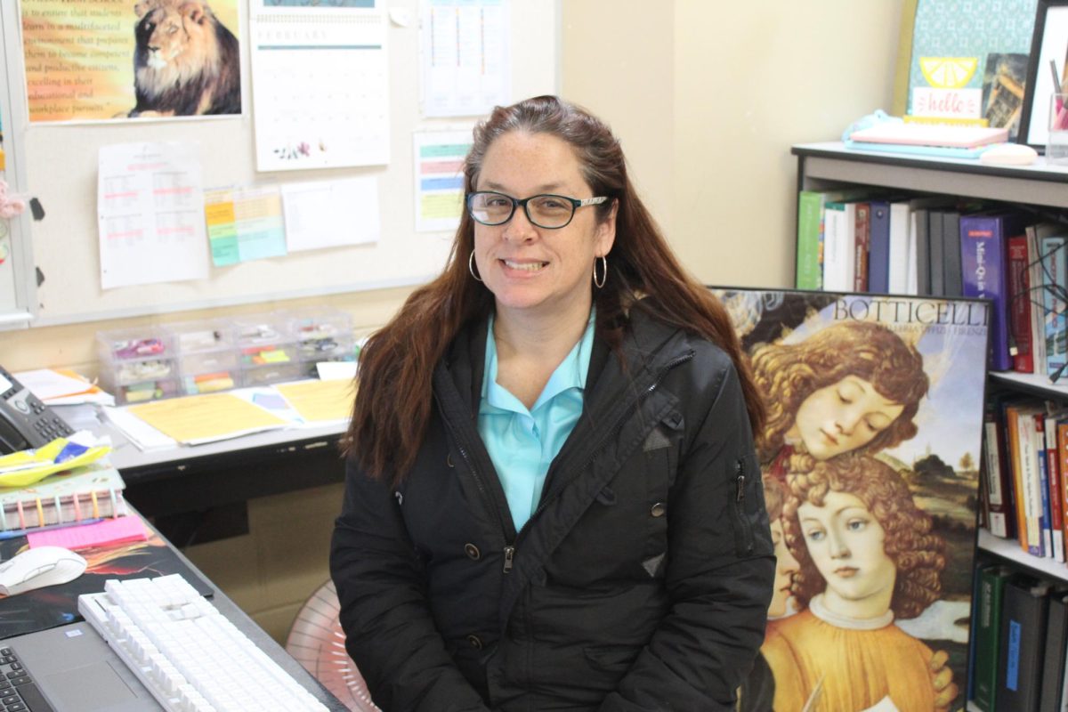 Verzaro poses behind her new desk. Behind her are canvases to be hung, a shelf, and just out of frame is a blue corkboard to be filled with photographic memories. 
