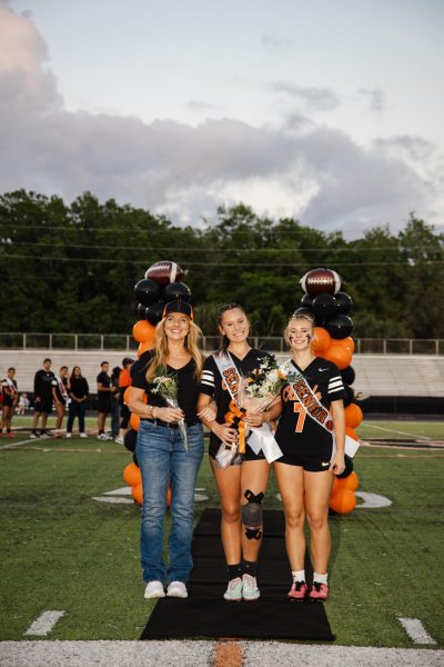 Senior Jules Decesare poses on the field with a bouqet arrangement during her senior night, surrounded by mother April Sevrino to her left and younger sister Gabriella Decesare to her right.